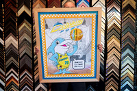 Colourful Dolphins basketball cartoon artwork featuring a dolphin mascot, custom framed in a wide natural timber frame in Port Macquarie.
