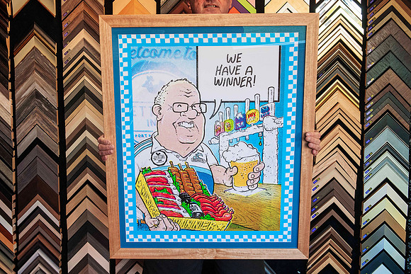 Colourful Australian cartoon artwork featuring a pub scene and the words We Have a Winner, custom framed in a wide natural timber frame in Port Macquarie.
