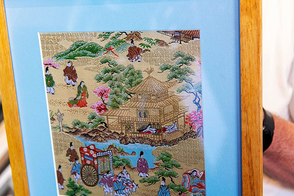 Close-up of detailed Asian embroidered textile showing traditional architecture, figures and landscape, custom framed with blue matboard and natural timber frame in Port Macquarie.