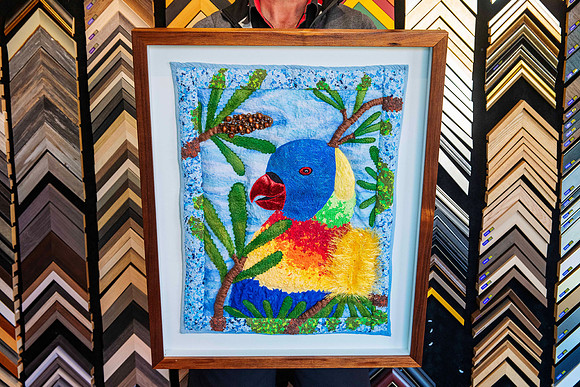 Colourful handmade textile parrot artwork with embroidery and textured fibres, professionally custom framed with a pale blue background and timber frame in Port Macquarie.