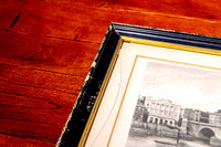 Older framed artwork with broken glass and aged orange-brown matboard core brought in for glass and mat replacement during professional frame repair in Port Macquarie.