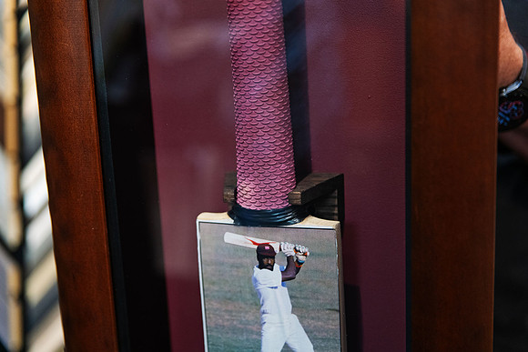 Close-up of custom framed signed Sir Viv Richards cricket bat showing the grip, secure mounting and cricket photograph against a burgundy background in a timber shadow box frame.