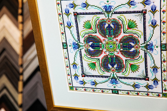 Close-up of intricate blue, green and gold beaded needlework with detailed stitching, custom framed with a neutral surround and gold-toned frame in Port Macquarie.