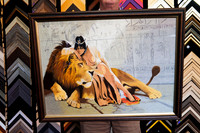 Detailed Egyptian-inspired textile artwork featuring a reclining lion and figure with hieroglyphic imagery, custom framed in a dark brown timber-look picture frame.