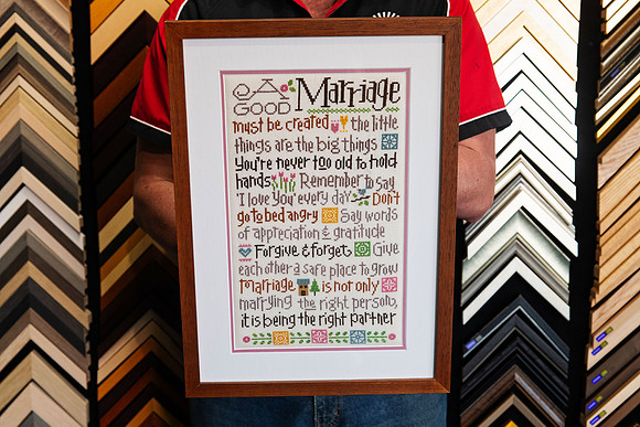 Marriage-themed handmade cross stitch custom framed with a white mat, pink accent and warm timber picture frame by Sunset Framing & Gallery in Port Macquarie.
