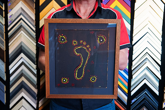 Hand-painted dot artwork with central footprint float mounted on a dark mat and custom framed in warm timber by Sunset Framing & Gallery Port Macquarie.
