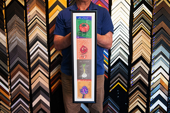 Four colourful travel prints arranged vertically in a long narrow black custom frame with white surround.