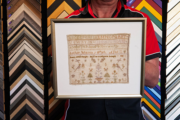 Vintage stitched sampler found inside an old book, custom framed with its original irregular textile edges visible in Port Macquarie.