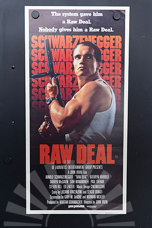 Raw Deal Australian Daybill showing Arnold Schwarzenegger in a grey singlet holding a firearm, against repeated red-orange surname lettering and a large red title.