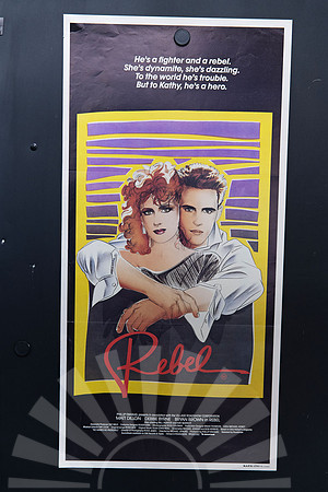 Rebel Australian Daybill featuring an illustration of Matt Dillon embracing red-haired Debbie Byrne, surrounded by a yellow frame, purple detailing and a red script title on a dark background.