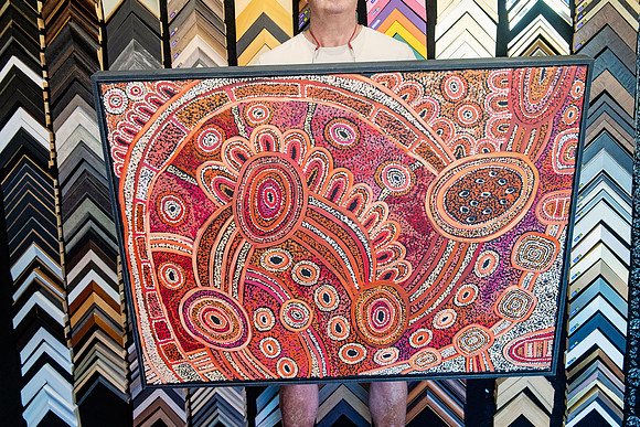 Large Aboriginal artwork in orange, red and pink tones finished with a slim dark frame.