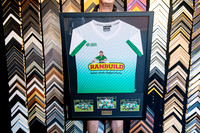 White sports jersey framed with three team photographs and presentation plaque.
