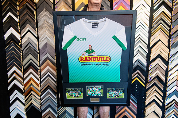 White sports jersey framed with three team photographs and presentation plaque.