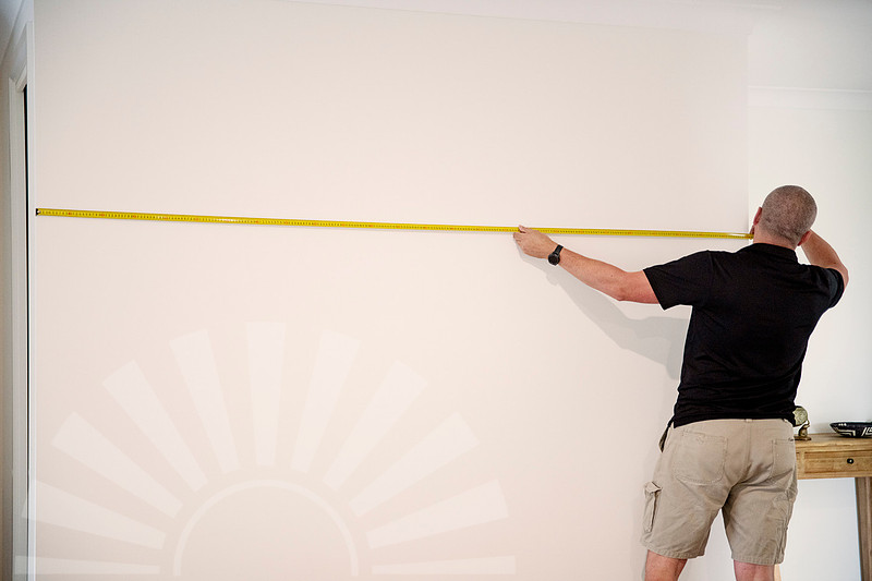 Framer Scott measuring a wall before professional artwork installation in a Port Macquarie home.